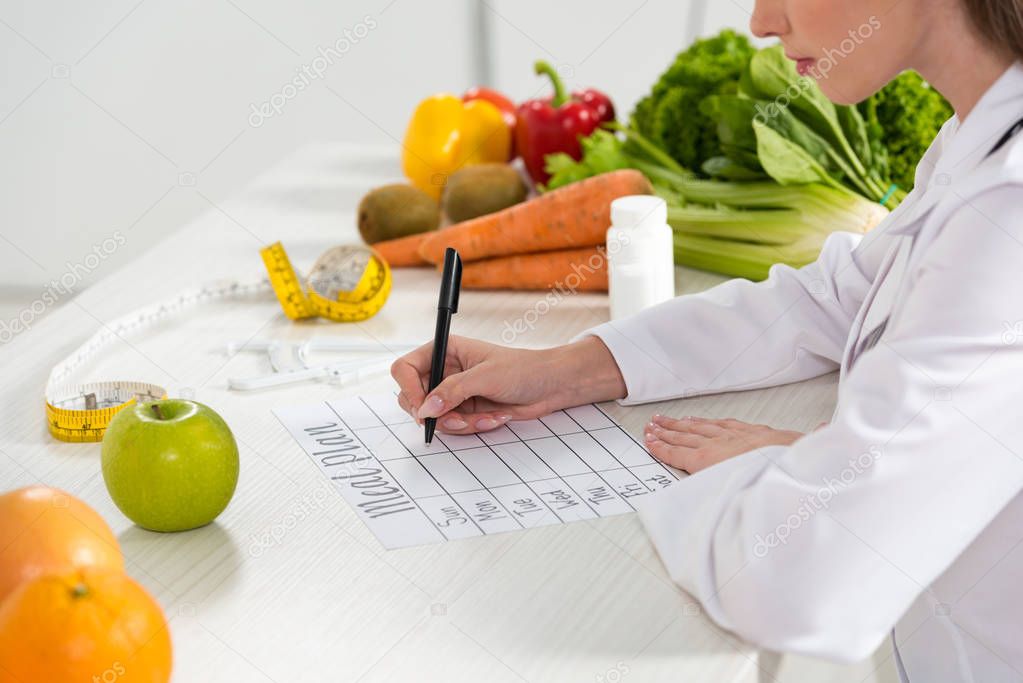 cropped view of dietitian writing in meal plan at workplace