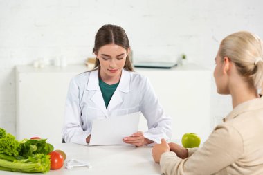 dietitian in white coat holding paper and patient at table clipart