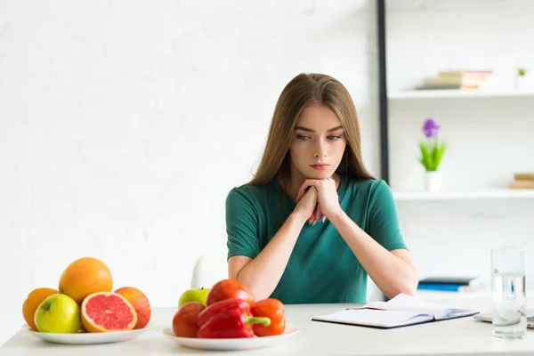 新鮮な果物や野菜とテーブルに座っている悲しい女性 — ストック写真