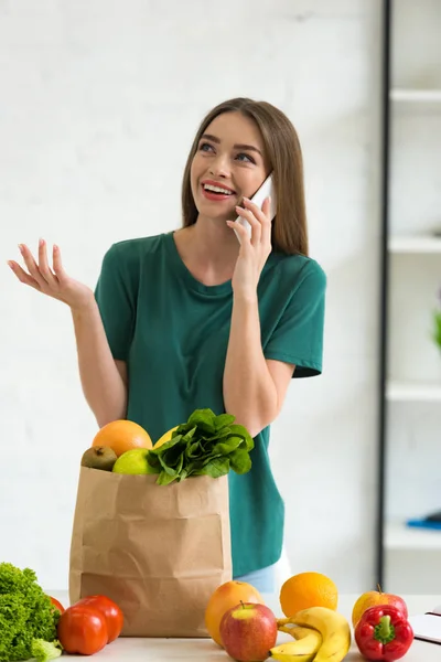 Uśmiechnięta Dziewczyna Stoi Pobliżu Worek Papierowy Świeżą Żywnością Rozmawiać Smartphone — Zdjęcie stockowe