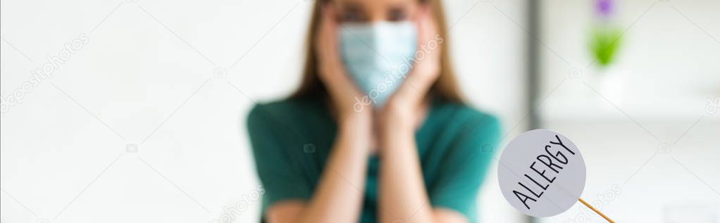 panoramic shot of woman in medical mask propping face with hands and nameplate with inscription allergy