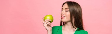 panoramic shot of attractive smiling girl holding green apple isolated on pink clipart