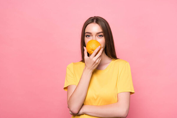 front view of attractive girl holding orange isolated on pink