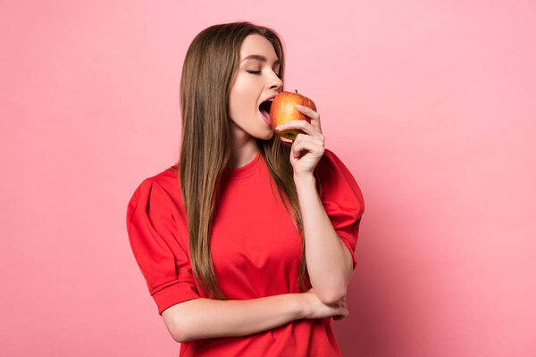 attractive young woman eating apple with closed eyes on pink