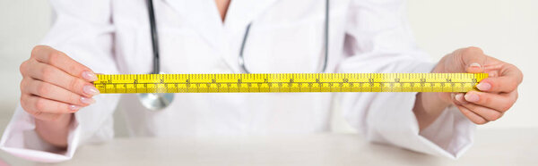panoramic shot of dietitian in white coat with stethoscope holding measure tape