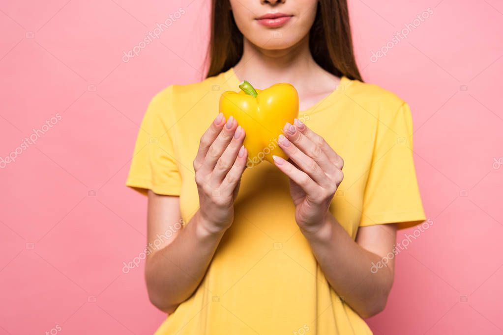 Cropped view of young woman in t-shirt holding yellow bell pepper on pink