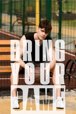 bring your game lettering on photo of sportsman with ball sitting on bench at basketball court clipart
