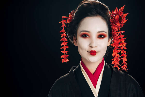 cheerful beautiful geisha in black and red kimono and flowers in hair isolated on black