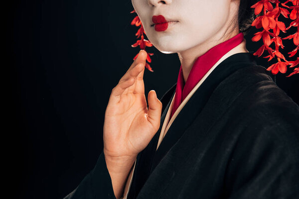 partial view of beautiful geisha in black and red kimono waving hand isolated on black