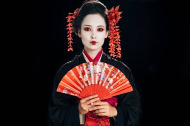 beautiful geisha in black kimono with red flowers in hair holding traditional hand fan isolated on black clipart