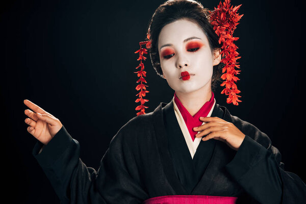 beautiful geisha in black and red kimono and flowers in hair gesturing isolated on black with copy space