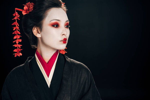 beautiful geisha in black and red kimono and flowers in hair looking away isolated on black