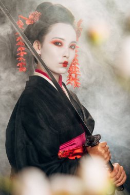 duman ve sakura dallarında katana tutan siyah kimono ciddi geyşa seçici odak