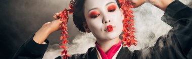 duman, panoramik çekim ile siyah arka plan üzerinde gesturing saç kırmızı çiçekler ile siyah kimono güzel geyşa
