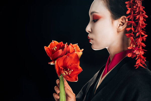 side view of beautiful geisha in black kimono with red flowers isolated on black