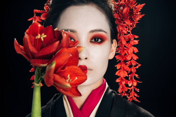 portrait of beautiful geisha in black kimono with red flowers isolated on black