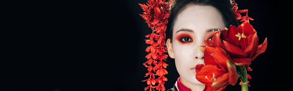 portrait of beautiful geisha in black kimono with red flowers isolated on black, panoramic shot