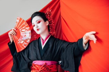 beautiful geisha in black kimono with hand fan and red cloth on background dancing isolated on white clipart