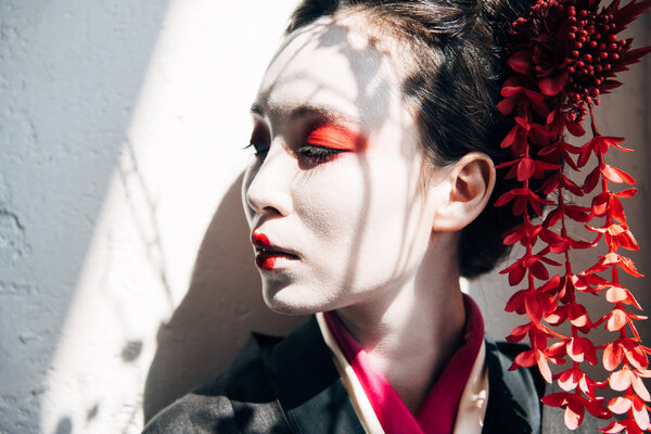 portrait of beautiful geisha with red and white makeup in sunlight with shadows