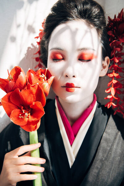 portrait of beautiful geisha holding red flowers in sunlight