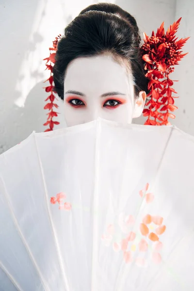beautiful geisha with red and white makeup holding umbrella in sunlight