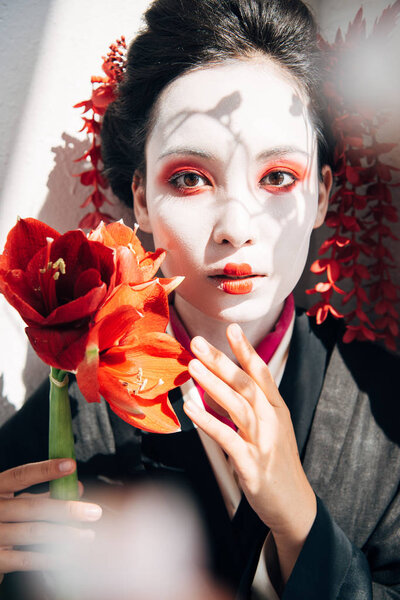 portrait of beautiful geisha holding red flowers in sunlight