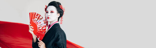 красивые гейши в черном кимоно с ручным вентилятором и красной тканью на заднем плане изолированы на белом с копировальным пространством, панорамный снимок
