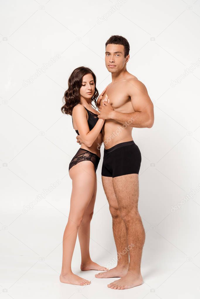 handsome mixed race man hugging woman in black underwear on white 