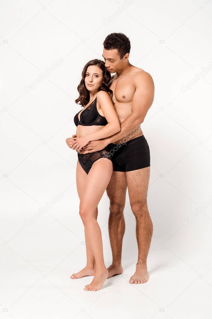 shirtless mixed race man hugging woman in black underwear on white 