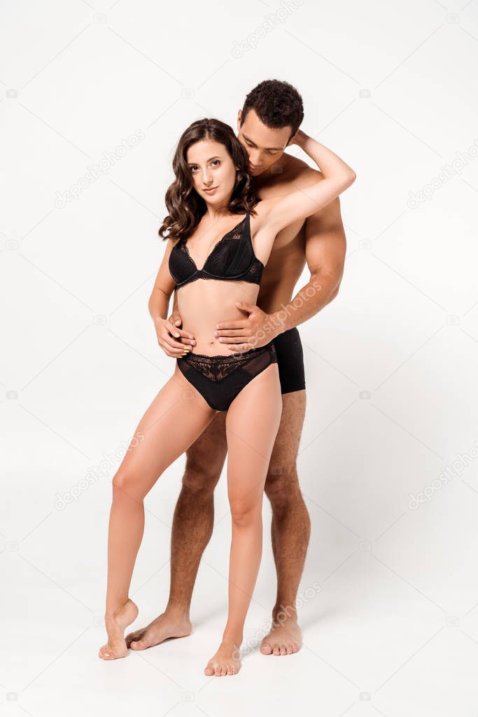 sexy mixed race man looking at seductive woman in black underwear on white 