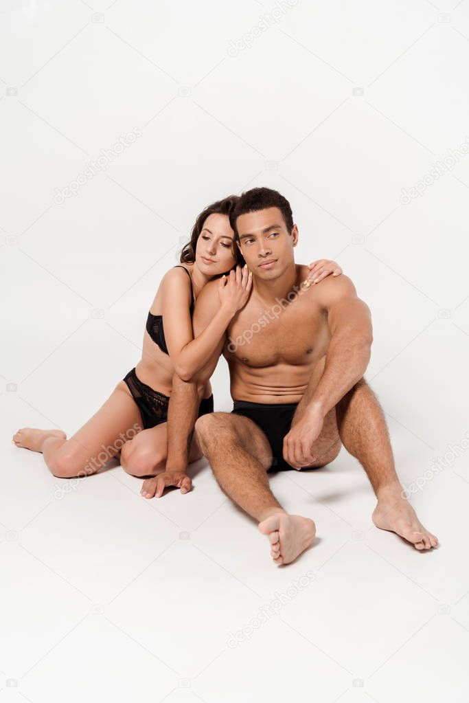 young woman in underwear hugging shirtless mixed race man while sitting on white 