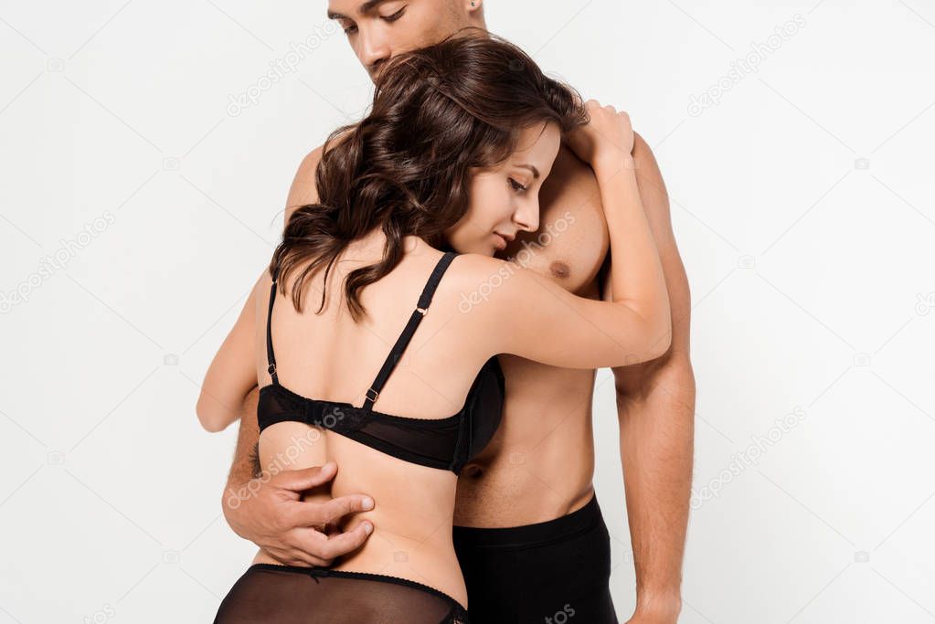 young woman in black underwear hugging shirtless mixed race man isolated on white 