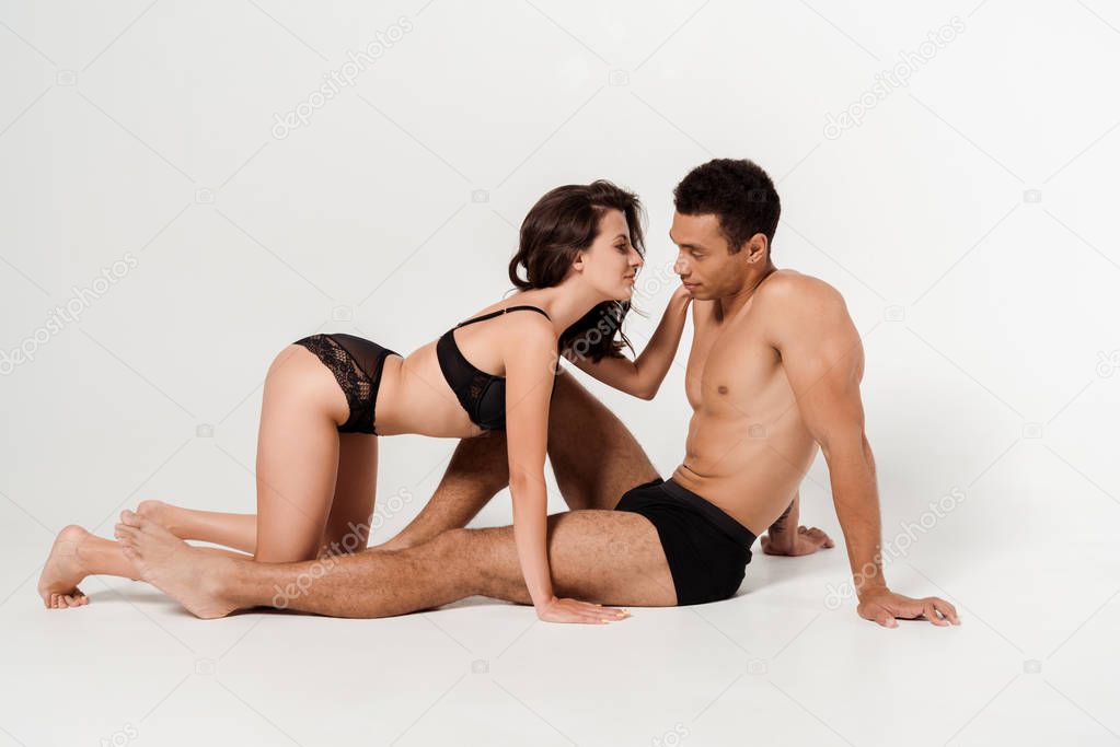 sexy girl in black underwear looking at muscular mixed race man sitting on white 