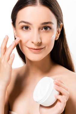 beyaz izole yüz kozmetik krem uygulayarak mükemmel bir cilt ile güzel genç gülümseyen kadın