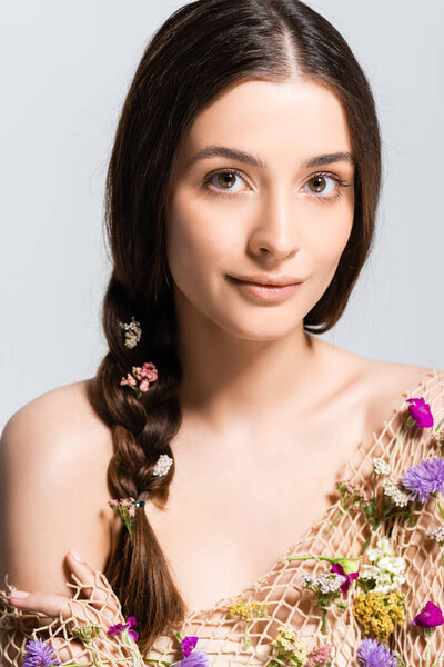 beautiful woman with braid in mesh with spring wildflowers looking at camera isolated on grey