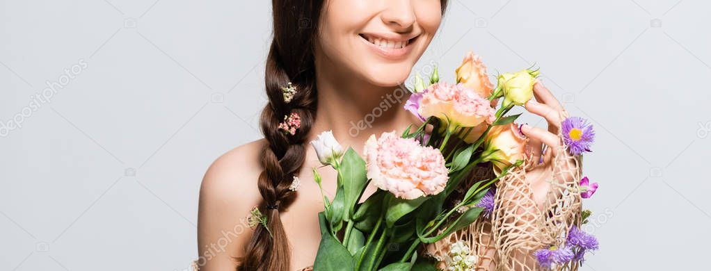 cropped view of happy beautiful woman with braid in mesh with spring wildflowers isolated on grey