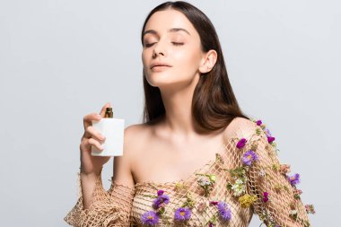 beautiful woman in mesh clothing with purple flowers spraying perfume with floral scent on skin isolated on grey clipart