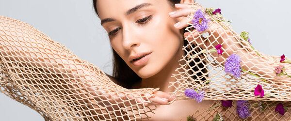 beautiful gentle woman in mesh beige clothing with purple flowers posing isolated on grey