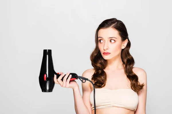 Unpleased Beautiful Brunette Woman Curls Makeup Holding Hairdryer Isolated Grey — стоковое фото