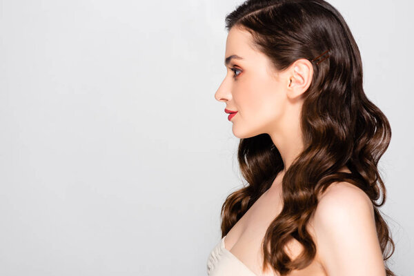 side view of beautiful brunette woman with curls and makeup isolated on grey