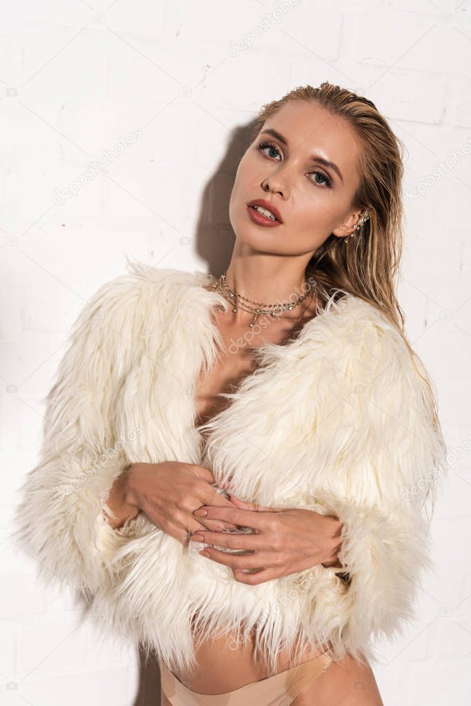 sexy half-naked young woman with wet hair in white faux fur coat on white background