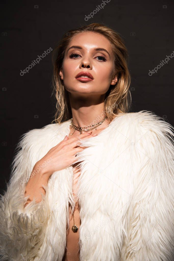 sexy young woman with wet blonde hair in faux fur coat isolated on black
