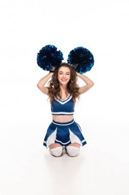 sexy happy cheerleader girl in blue uniform sitting on floor and holding pompoms near head isolated on white clipart