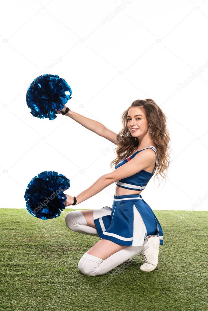 side view of sexy happy cheerleader girl in blue uniform with pompoms dancing on grassy field isolated on white