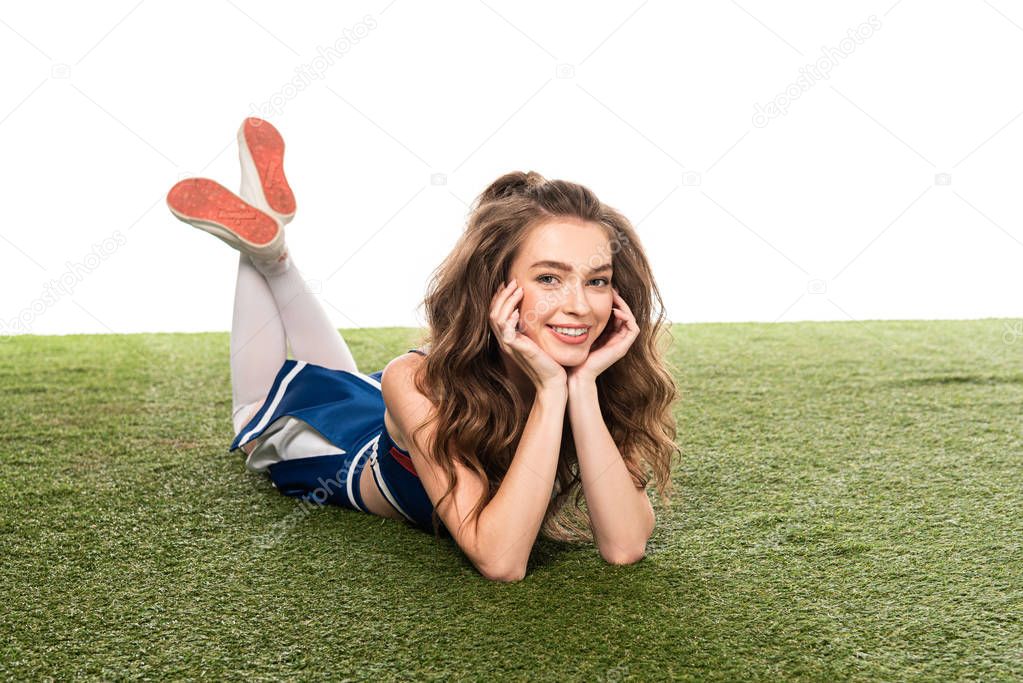 smiling cheerleader girl in blue uniform lying on green field isolated on white