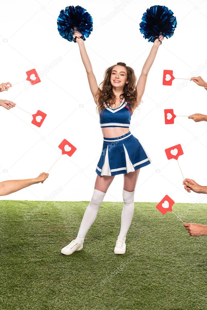 happy cheerleader girl in blue uniform with pompoms standing on green field with people hands holding likes around isolated on white