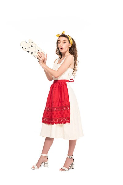 full length view of young shocked housewife in dress and apron holding oven mitten isolated on white