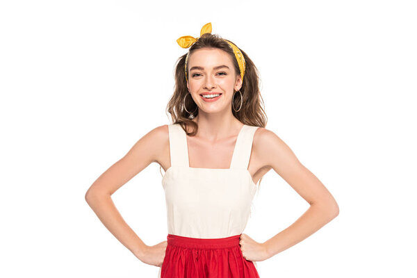 young smiling housewife in dress and apron standing akimbo isolated on white