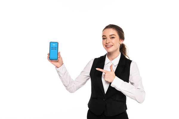 KYIV, UKRAINE - APRIL 7, 2019: happy young waitress pointing with finger at skype app on smartphone isolated on white