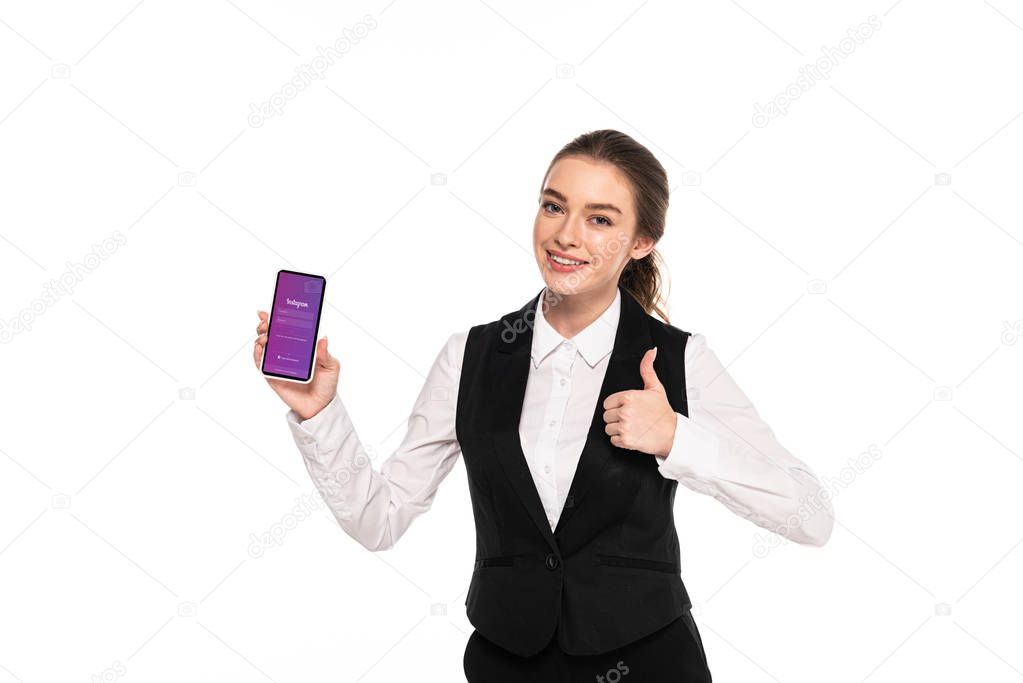 KYIV, UKRAINE - APRIL 7, 2019: happy young waitress holding smartphone with Instagram app and showing thumb up isolated on white